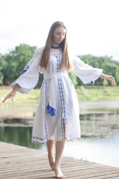 a girl in an embroidered Ukrainian shirt sits on the pier, the reflection of clouds in the water of the lake. On the shore of the sky. vyshyvanka day. freedom. patriot.