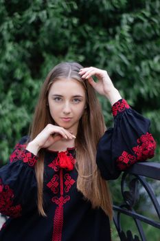 charming ukrainian young woman in embroidered national red and black dress outdoors. pretty girl in park wearing vyshyvanka.