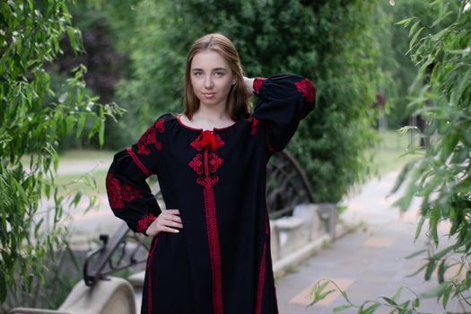girl in national traditional ukrainian clothes. black and red embroidered dress. woman model posing in park outdoors.