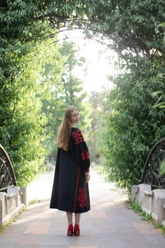 girl in national traditional ukrainian clothes. black and red embroidered dress. woman model posing in park outdoors.