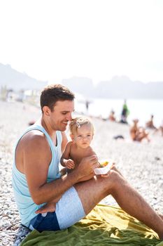 Dad feeding his little daughter sitting on the beach. High quality photo