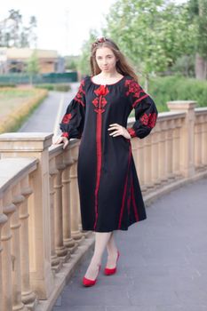 charming ukrainian young woman in embroidered national red and black dress outdoors. pretty girl in park wearing vyshyvanka.