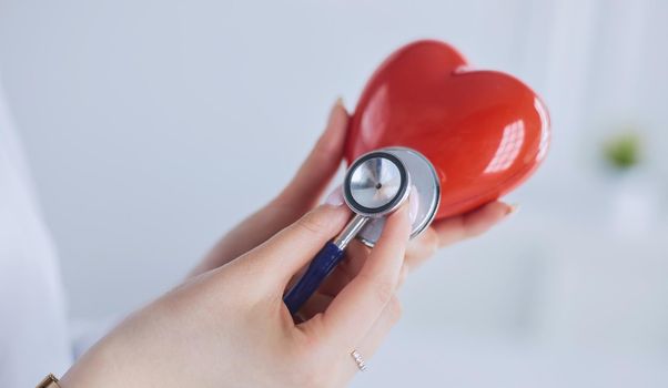 A doctor with stethoscope examining red heart, isolated on white background.