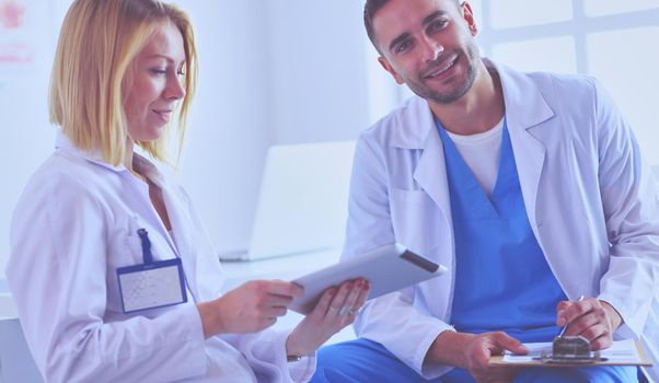 Handsome doctor is talking with young female doctor and making notes while sitting in his office