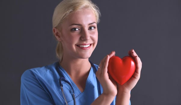Female doctor with stethoscope holding heart, isolated on grey background
