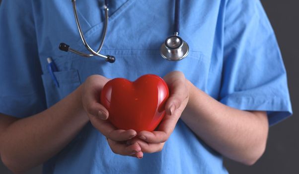 Female doctor with stethoscope holding heart, isolated on grey background