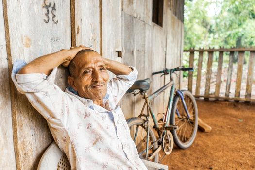 Latin grandfather with arms above his head relaxing in his poor house in El Rama Nicaragua