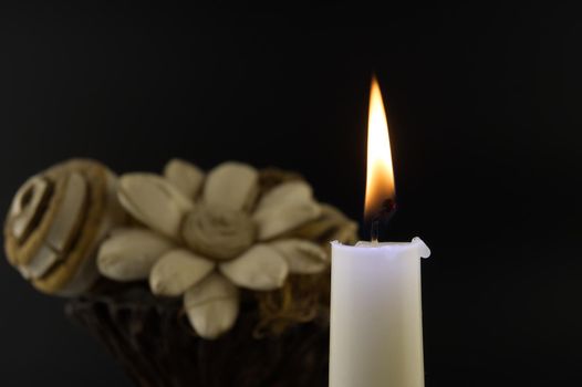 Close-up of a burning candle and flowers illuminated by the candlelight in the darkness with free copy space