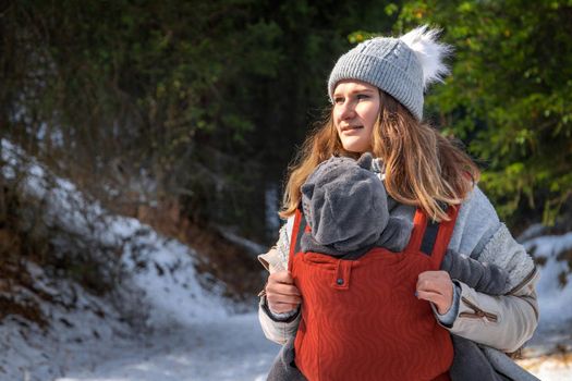 Babywearing young mother with her baby winter outdoor adventure with copy space.