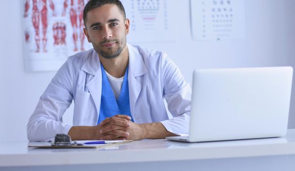 Portrait of a male doctor with laptop sitting at desk in medical office
