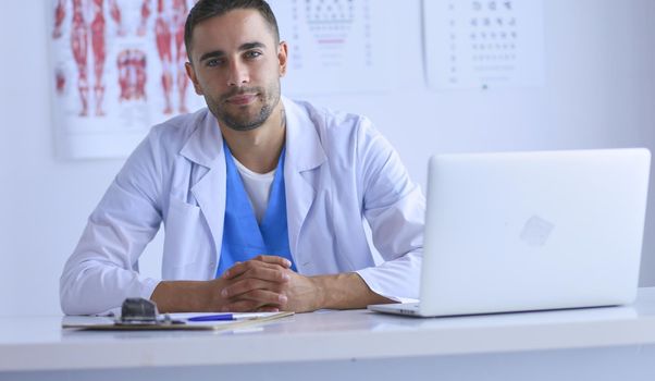 Portrait of a male doctor with laptop sitting at desk in medical office