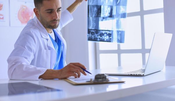 Handsome doctor is talking with young female patient and making notes while sitting in his office