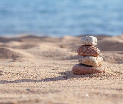 Round stones lie on top of each other in a column on the seashore on a sunny summer day. The concept of order and tranquility