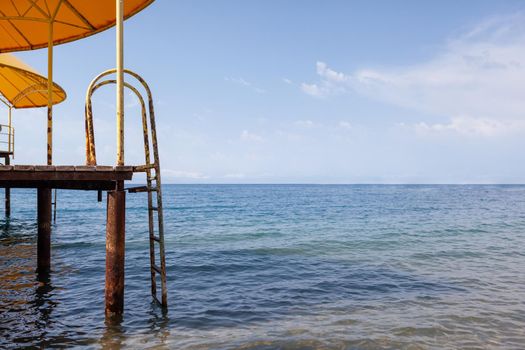 Swimming area or pier on the sea. A large pier with a roof, wooden planks and rusty stairs descending into the water. Bathing and resting place.