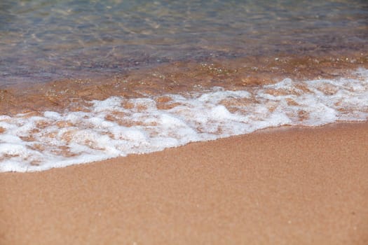 A soft wave runs on a sandy shore on a summer day. Empty space can be used as background for display or montage your top view products.