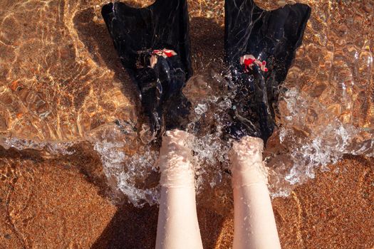 A woman in black flippers splashes near the shore. Fins stick out of the water. Swimming equipment. Summer holidays, fun, exploring the sea world concept. Space for copy.