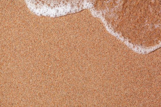 A soft wave runs on a sandy shore on a summer day. Empty space can be used as background for display or montage your top view products.