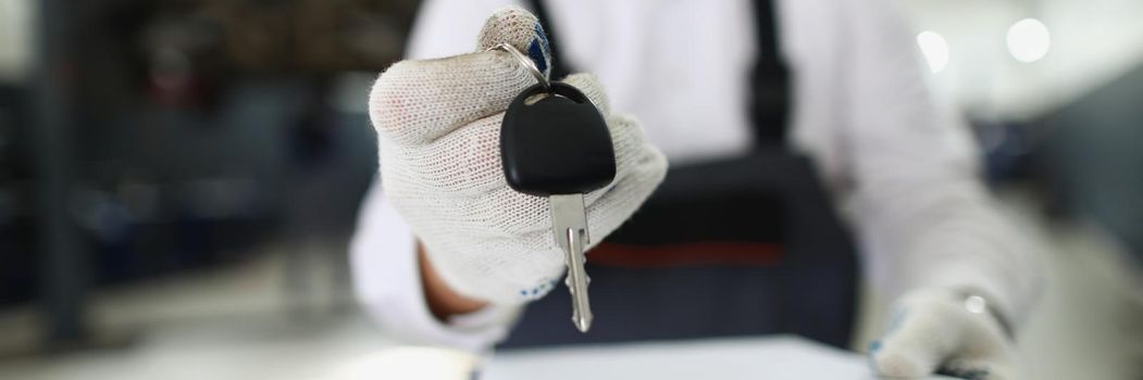 Close-up of service worker give keys from fixed automobile to owner and hold paper for sign. Car service, professional mechanic, garage, pit stop concept