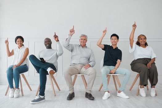 Portrait of a diverse group of people pointing up while sitting in line against a white background.