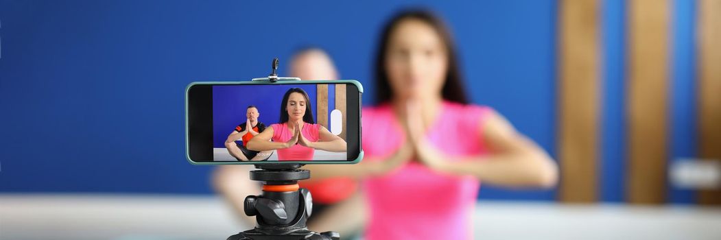 Close-up of camera on tripod filming people perform asana on mat in studio. Morning ritual for body and soul health. Course, social media content concept