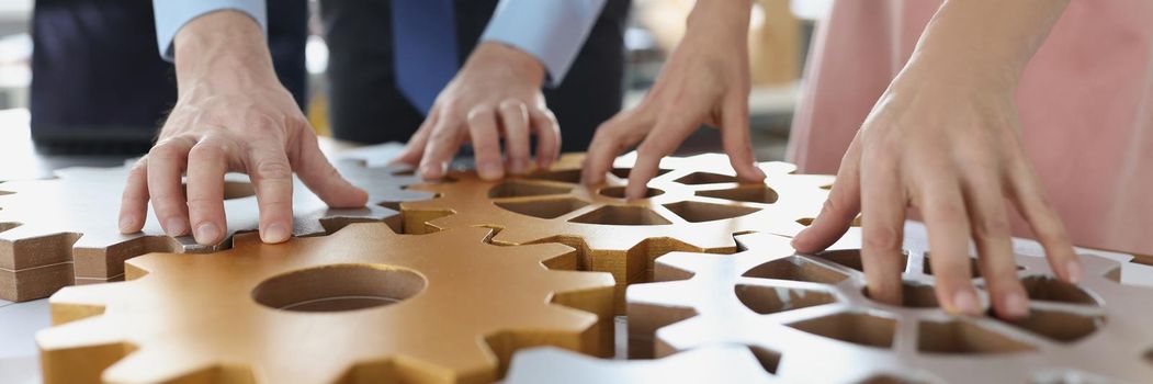 Close-up of business people making whole picture of wooden gears on workplace together in office. Teamwork, cooperation and successful development concept
