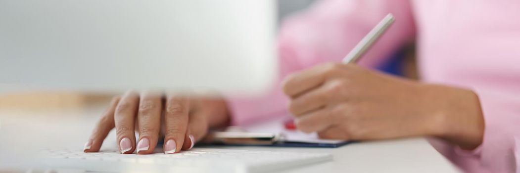 Close-up of person writing down ideas in journal on working place, making notes for future, planning day. Typing on keyboard at same time. Planner concept