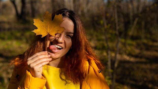 Red-haired Caucasian woman holding a fallen maple leaf. Autumn Walk