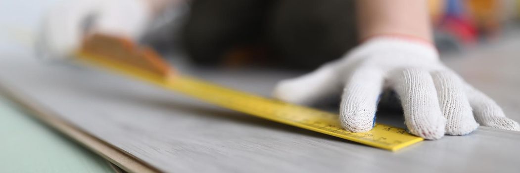 Close-up of professional male worker apply tape measure on wooden plank for further cutting. Foreman builder repair floor. Construction site, build concept