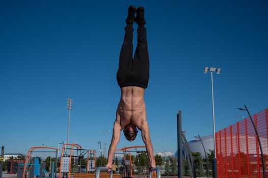 Shirtless man doing handstand on parallel bars at sports ground