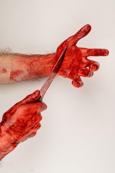 A man with bloody hands cuts himself with a knife