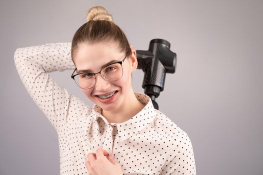 Smiling woman with braces uses a massager gun for her back