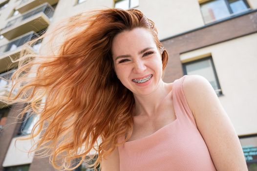 Beautiful young red-haired woman with braces on her teeth smiling in the summer outdoors.