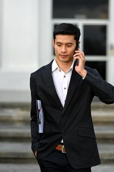 Handsome asian businessman talking on mobile phone while walking down on the stairs of an office building.