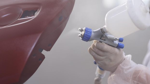 Painter paints the red car in garage. car painting with professional spray gun. Master is painting part of automobile in car service.