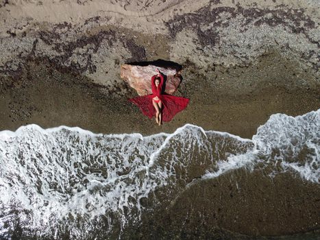 Young sensual blonde woman sitting on the rock near water at sea and enjoys the sea waves on background of two volcanic rocks, like in Iceland. Dreams holidays and weekend vacation in summer time