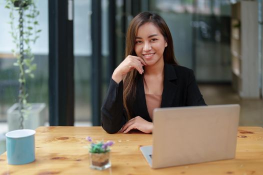 Portrait of a beautiful Asian businesswoman in a formal suit sits at her office desk with laptop computer in office.