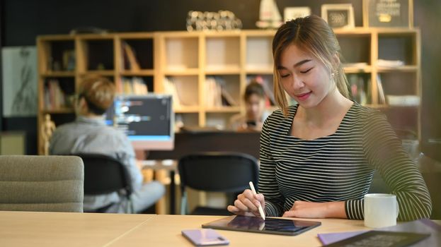 Young female software programmer or coder working in startup company and colleagues sitting in background.