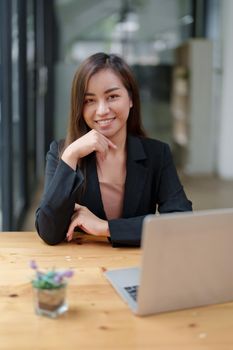 Portrait of a beautiful Asian businesswoman in a formal suit sits at her office desk with laptop computer in office.