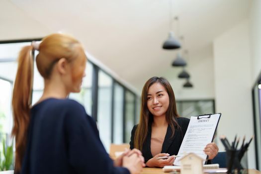 Portrait of an Asian female bank employee asking a customer to read the contract before signing to agree to buy a house, real estate concepts.