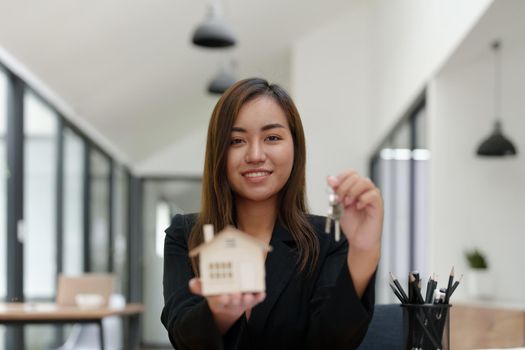 Portrait of an Asian female bank employee handing over a house and keys to a client after signing a contract on paperwork