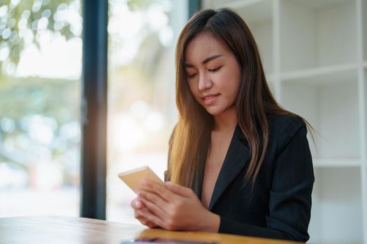 Portrait of an Asian female employee wearing a formal suit using a mobile smartphone to do business with coworkers.