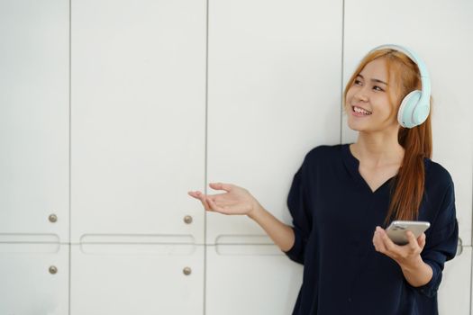 portrait of a young Asian woman with blonde hair wearing over-ear headphones listening to music for relax while taking a break from boring day activities.