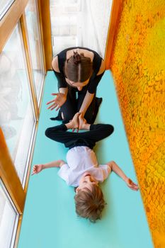 family sport. mother teaches son to do yoga. Helps with stretching. On the balcony In a home apartment.