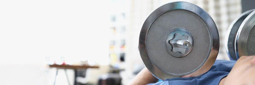 Close-up of man lift heavy metal dumbbell laying on training machine. Train body for muscles, healthy living, gym at home. Sport, active lifestyle concept