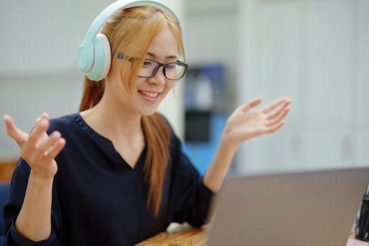 A portrait of a young Asian woman with blonde hair wearing over-ear headphones listening to music to relax while taking a break from boring day activities.