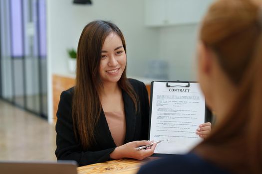 Portrait of an Asian female bank employee asking a customer to read the contract before signing to agree to buy a house, real estate concepts.