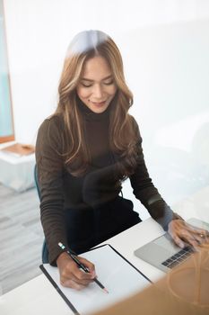 View through the window of female designer working with computer laptop in office.