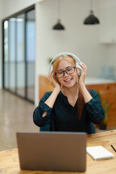 A portrait of a young Asian woman with blonde hair wearing over-ear headphones listening to music to relax while taking a break from boring day activities.