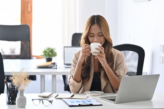 Attractive businesswoman sitting at her workplace drinking coffee in the morning.