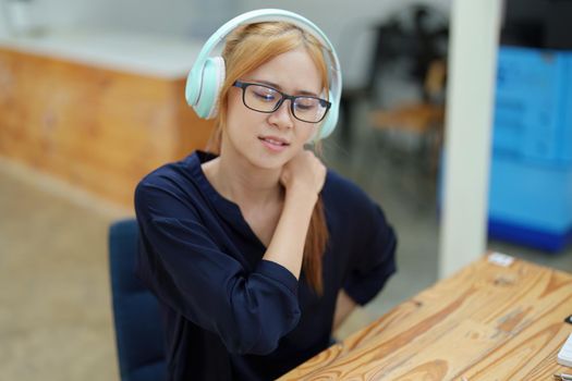 Portrait of an Asian teenage girl feeling pain in the neck muscles after working on a laptop computer for a long time. Office Syndrome concept.